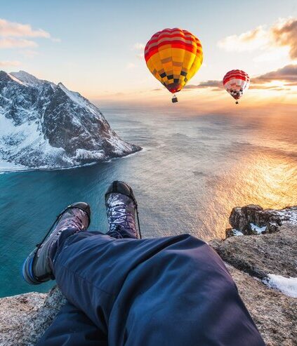 man hiker cross legs sitting rock ridge with hot air balloon flying ocean sunset_49071 3972 e1730210108284